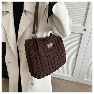 Vista detallada del bolso tote plisatdo marrón café con etiqueta de moda en modelo