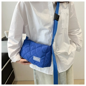 Detail of blue quilted nylon tote bag featuring Fashion label and adjustable shoulder strap