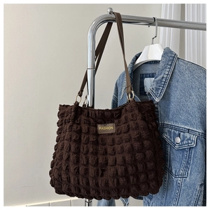 Detailed close-up of brown quilted textured tote bag featuring a gold fashion logo