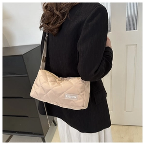 Detail of beige quilted shoulder bag featuring fashion label and wide strap