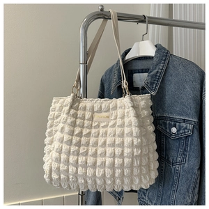 Detailed close-up of cream textured bubble tote bag with fashion tag on denim background