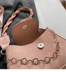Detail of pink faux suede bag featuring twisted strap and floral metal chain with magnetic clasp