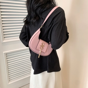 Pink crescent shoulder bag with gold logo and tassel charm worn by model in minimalist setting
