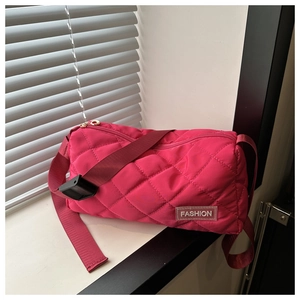 Detail of rose red quilted barrel bag with fashion tag and wide adjustable shoulder strap