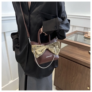 Détail d'un sac en cuir marron avec un grand nœud en velours vert et une chaîne perlée
