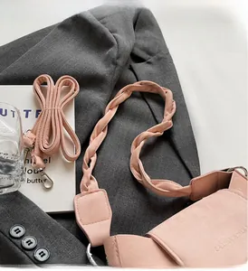 Close-up of pink matte leather crossbody bag with woven handle on a grey blazer