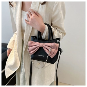 Détail du mini sac cabas en cuir noir avec un grand nœud en daim rose et chaîne