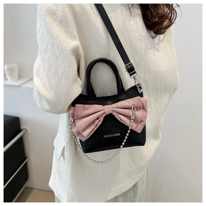 Détail du sac bandoulière noir avec grand nœud rose et chaîne à billes argentée