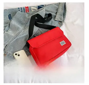 Detailed view of red canvas messenger bag next to a smartphone for size comparison
