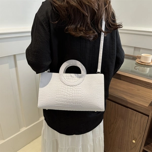 White crocodile embossed leather handbag with round handle shown on model in modern room