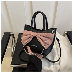 Détail d'un sac en cuir noir avec un grand nœud rose et une chaîne à billes argentée