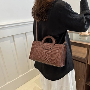 Brown crocodile embossed tote bag with unique circular handle shown on model in modern room