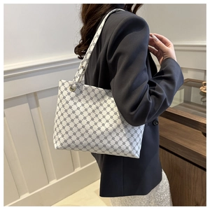 Side view of white monogram tote bag with geometric clover print carried by a model