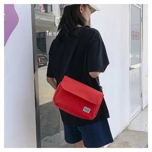 Red canvas messenger bag shown on back, featuring adjustable strap and minimalist brand tag