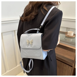 Detail of light blue textured leather backpack with metallic butterfly buckle on model