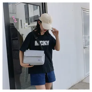 Outdoor shot of light grey casual crossbody bag with black adjustable strap and flap design