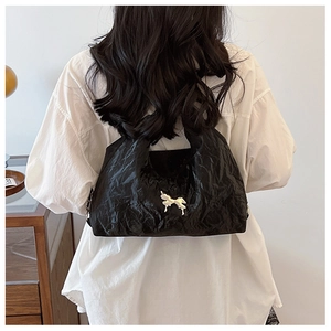 Detail of black pleated bucket bag with silver bow ornament worn by a model