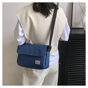 Blue canvas messenger bag with adjustable black strap worn by a model in casual setting