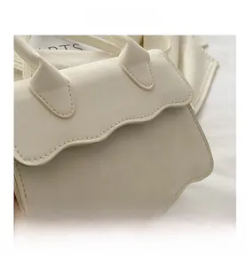 Detail view of cream mini handbag with unique wavy edge flap and matte leather texture