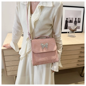 Detail of light pink flap handbag featuring a metallic silver butterfly buckle and thin strap