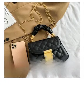 Detail of black quilted crossbody bag with gold buckle and chain next to a smartphone