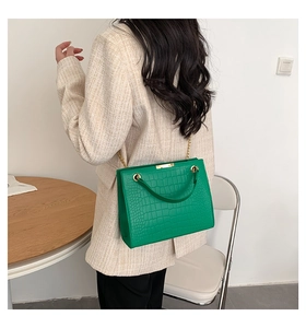 Close-up of green crocodile texture leather bag with elegant gold chain and hardware