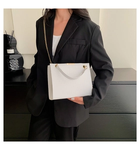 Close-up of white croc-effect shoulder bag with elegant gold chain on a black blazer