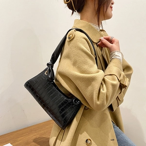 Classic black crocodile pattern underarm bag with knot strap on a beige coat model