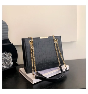 Detail of black crocodile texture bag with gold chain strap and metallic buckle