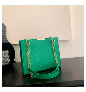 Detail of green crocodile embossed texture and dual golden chain straps on underarm bag