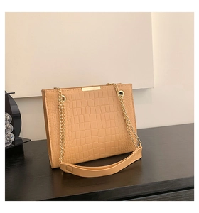 Close-up of light brown crocodile pattern leather bag with golden chain and metal hardware