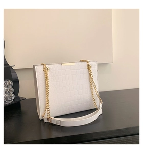Detail of white crocodile pattern tote bag with gold metal trim and chain strap