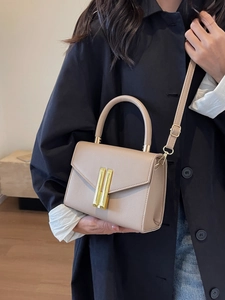 Minimalist beige textured leather crossbody bag with gold buckle on black coat