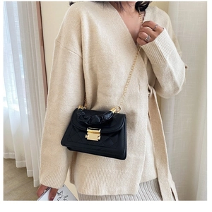 Quilted black crossbody bag with gold chain strap and gathered handle on beige knitwear