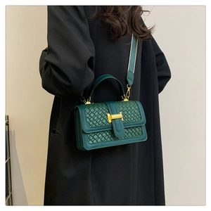 Model showing dark green plaid handbag with gold clasp and wide strap on black coat