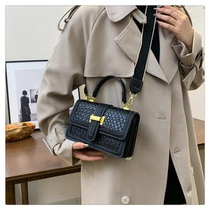 Detail of black woven texture handbag with gold hardware and wide shoulder strap