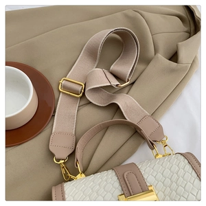 Close-up of cream textured faux leather bag with khaki trim and wide fabric strap