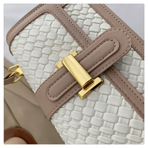 Detailed close-up of woven white fabric with tan leather trim and golden metal lock