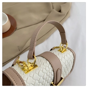 Detail of woven leather texture and gold hardware on white cylindrical handbag