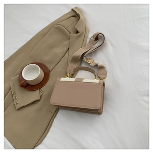 Detail of a square beige crossbody bag with woven leather flap and wide canvas strap