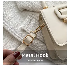Detail of golden metal hook and adjustable leather strap on a white shoulder bag