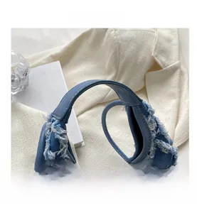Détail du sac seau en denim bleu avec bords effilochés blancs et fermoir rotatif argenté