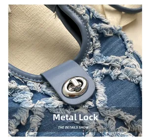 Gros plan du fermoir rotatif argenté sur un sac à main en denim bleu avec détails effilochés