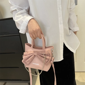 Sac à bandoulière rose avec nœud et chaîne argentée présenté dans un cadre élégant