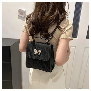 Detail of a chic black textured backpack featuring a silver liquid metal butterfly motif