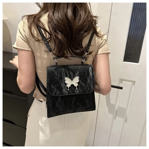 Detail of black pleated leather backpack with metallic butterfly buckle on female model