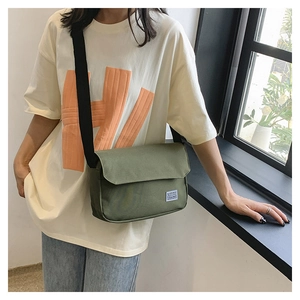 Side view of a large green canvas messenger bag on white T-shirt with adjustable strap