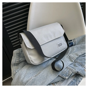 Detail of light gray canvas messenger bag with brand label on a denim jacket background