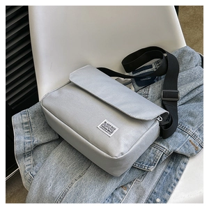 Close-up of light gray canvas messenger bag with adjustable strap on denim jacket