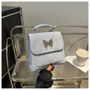 Detail of light blue wrinkled texture bag with metallic silver butterfly clasp on a stand